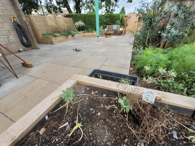 Garden landscaping project in Mells with Hardwood Balau Deck, Kandla Grey Sandstone Paving, Flowerbeds, Scottish Pebbles, and Slatted Fence Panels